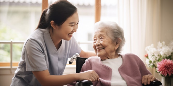 車椅子の高齢女性と目線を合わせ、笑顔で手を取り合う女性スタッフの様子