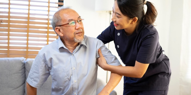 高齢男性の体を支えながら、笑顔でサポートしている女性スタッフの様子