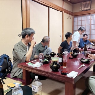 和室の広間でおこなわれた社内懇親会で、食事やお酒を囲みながら談笑する社員たち